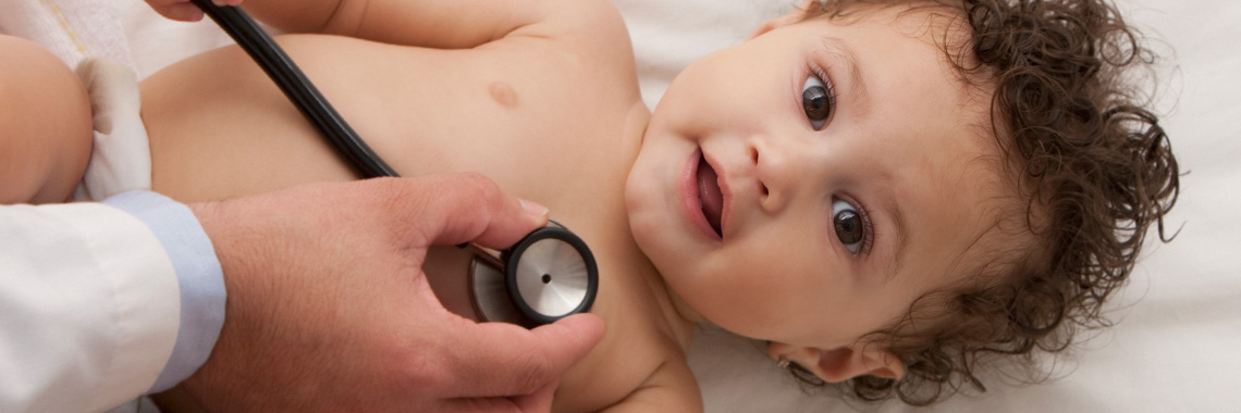 Ein Baby liegt mit dem Rücken am Boden und blickt interessiert nach oben. Ein Doktor in weißem Kittel hört zeitgleich den Herzschlag des Babys ab.