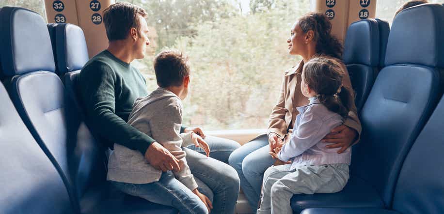 Eine vierköpfige Familie sitzt in einem Zugabteil und blickt aus dem Fenster. Die beiden Kinder lehnen sich an ihre Eltern und werden von ihnen umarmt.