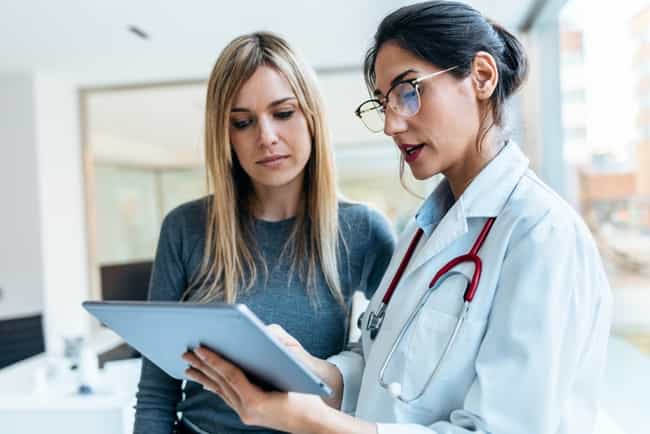 Ärztin mit Stethoskop bespricht und zeigt einer Patientin in der Praxis, die Ergebnisse