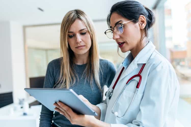 Ärztin mit Stethoskop bespricht und zeigt einer Patientin in der Praxis, die Ergebnisse