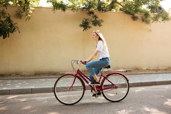 Eine Frau fährt auf einem roten, älteren Fahrrad. Sie fährt auf einer betonierten Straße und schaut gerade aus.