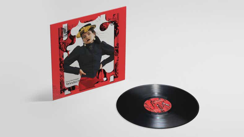 Das Cover eines Albums steht links neben einer schwarzen Vinylplatte. Das Cover hat einen roten Rand und in der Mitte ist eine junge Frau mit schwarzem Oberteil und Hut abgebildet.