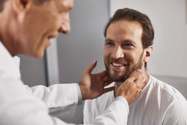 Ein Arzt steht vor seinem Patienten und greift ihm seitlich auf den Hals. Beide lächeln entspannt.