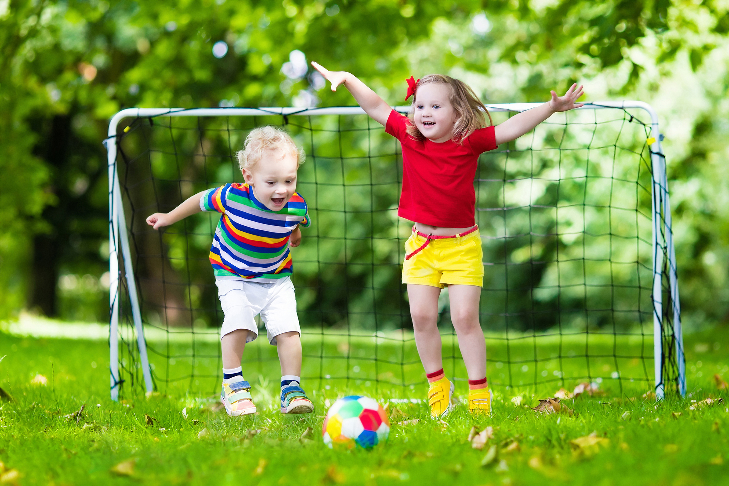 Child playing football. Kids play soccer on outdoor pitch. Little boy and girl kicking ball in summer park. Healthy activity for young children. School sport club team. Football junior league.