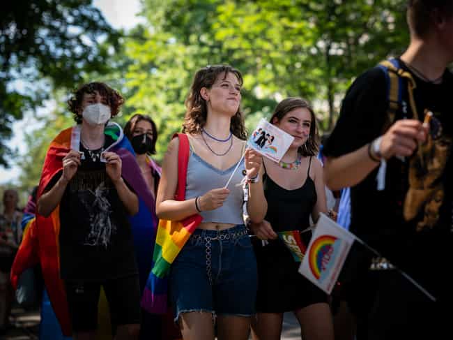 Junge Menschen nehmen an der Vienna Pride Parade teil. Sie tragen Regenbogenflaggen, lächeln und halten Pride-Schilder in den Händen.
